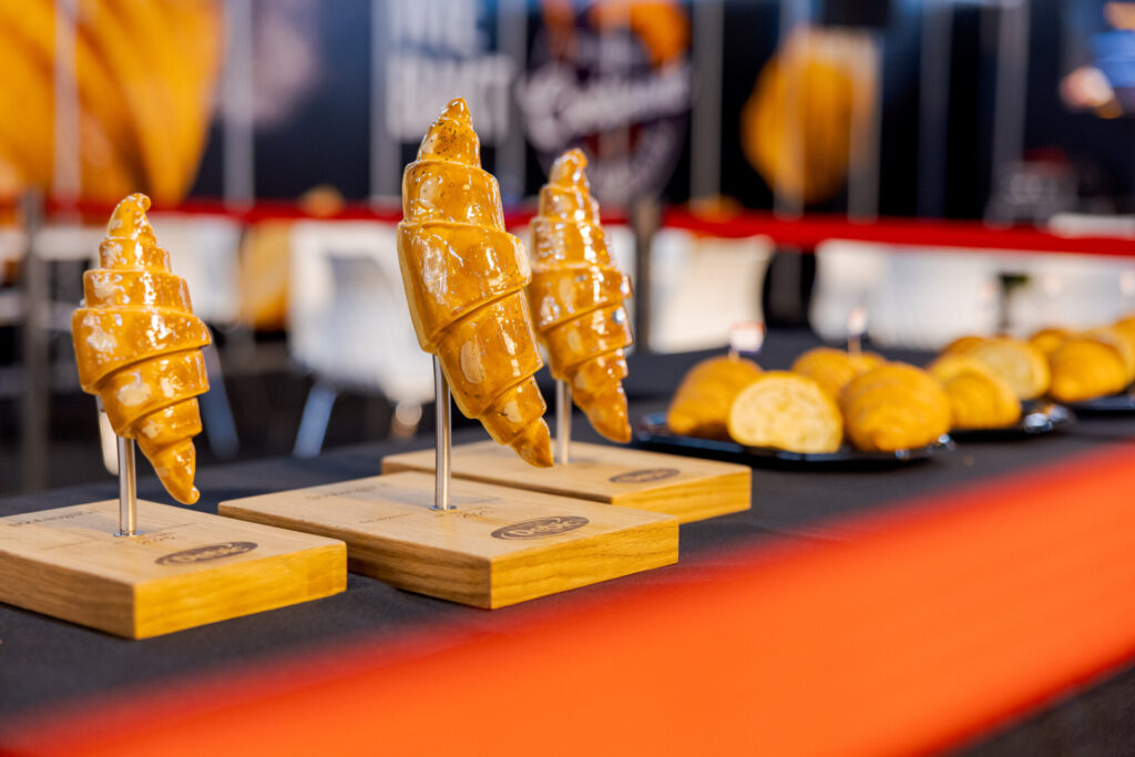 Drie glanzende croissantsculpturen op houten sokkels op Bakkersvakbeurs