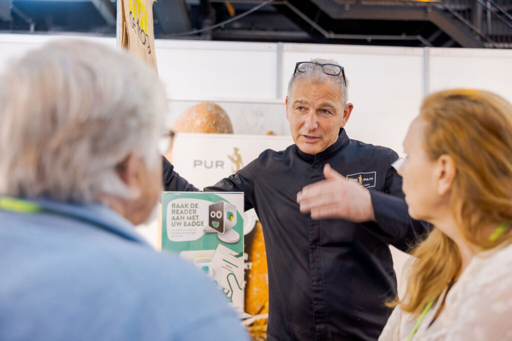 Bakker spreekt met bezoekers op een beursstand bij Bakkersvak & IJs-Vak