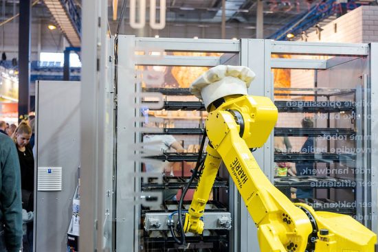 Gele industriële robotarm met koksmuts op Innnovatiezone Bakkersvakbeurs & IJs-Vak