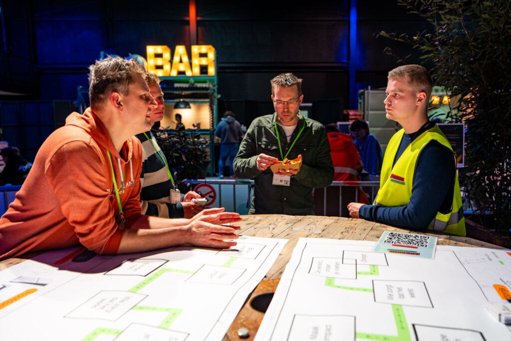Vier mannen bespreken plattegronden aan een tafel bij een bar