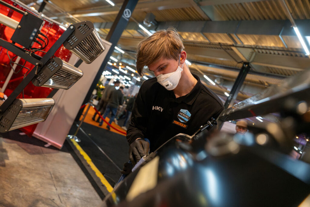 Monteur met mondmasker werkt aan auto op beurs