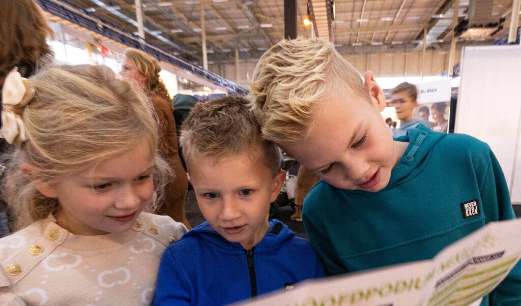 Drie kinderen lezen brochure op beurs