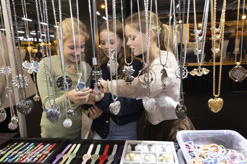 Drie meisjes bekijken sieraden bij een marktkraam