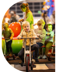 Kinderen spelen op driewielers tijdens een indoor evenement