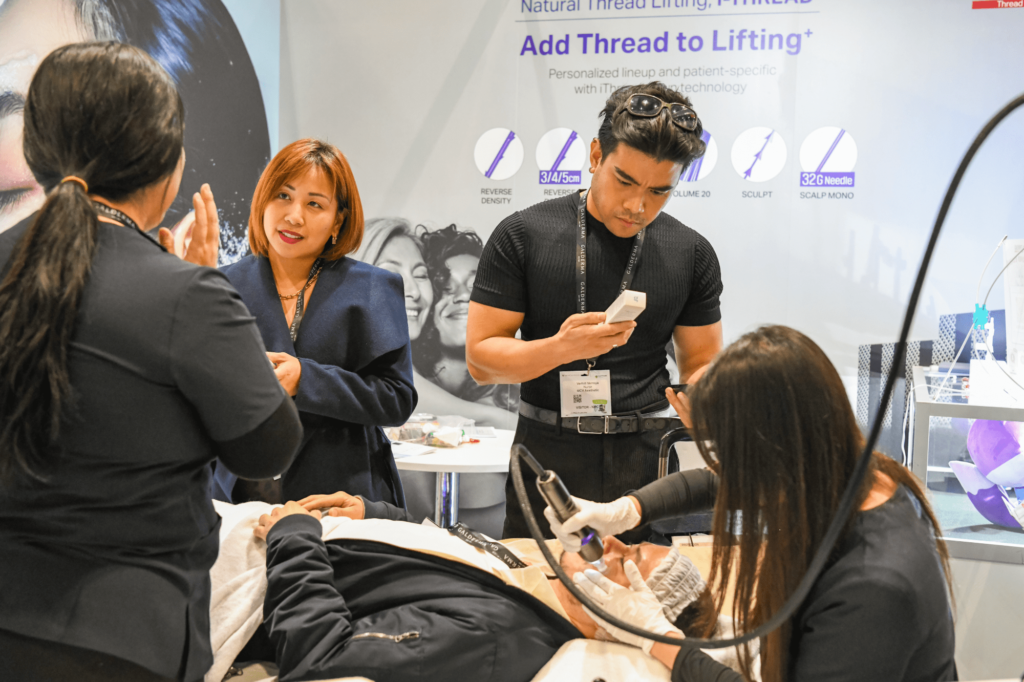 A person is laying have a facial treatment done while 3 people are talking behind the demo