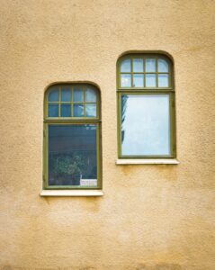 Twee afgeronde ramen met olijfgroene kozijnen op een gele buitengevel.