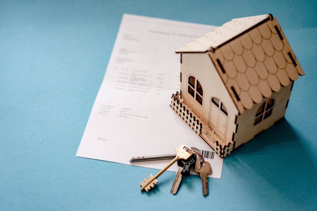 Een miniatuur houten huisje op een papier met daarnaast een sleutelbos.