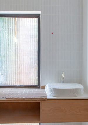 Badkamer die gerenoveerd wordt met plastic dekzeilen over de lavabo en het raam.