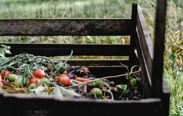 Foto van een houten compostbak in een tuin met daarin groente- en fruitafval.
