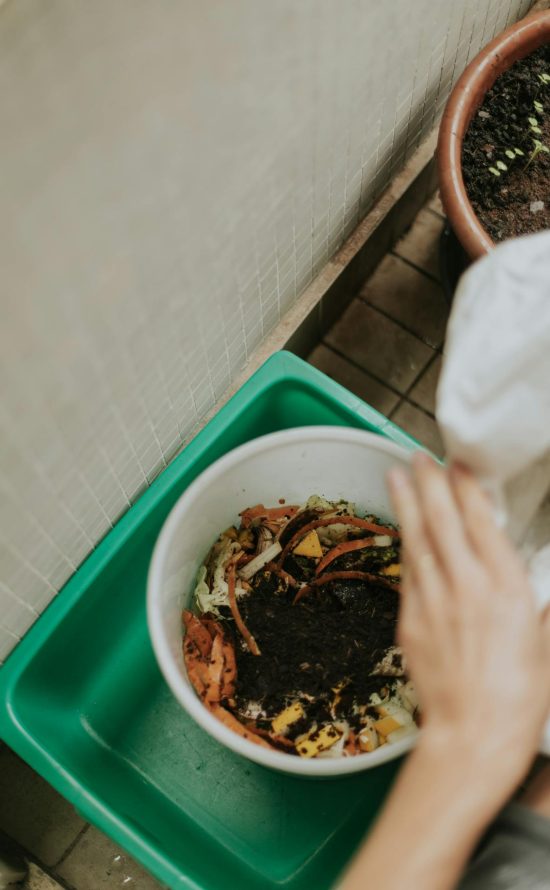 Foto van iemand die hun groenteafval in een emmer leegt.