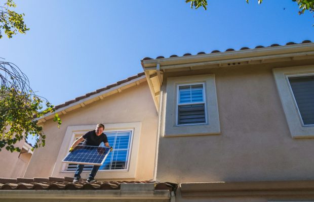 Energieneutrale woning pexels-Kindel Media Een man op het dak van een huis die een zonnepaneel draagt
