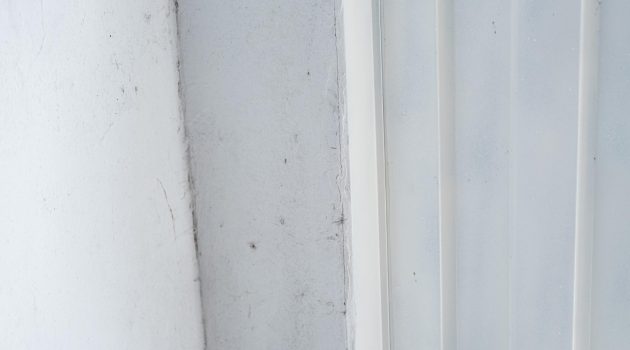 De hoek van een raamkozijn met subtiele schimmel erop.