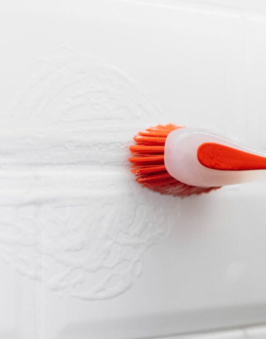 Voegen van witte muurtegels die met een oranje borstel gekuist worden.