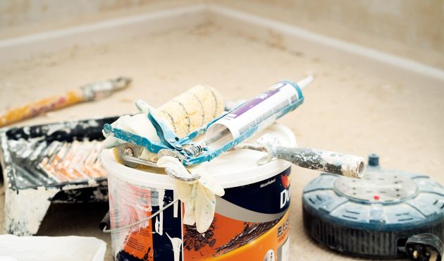 Hoek van een badkamer met werkmateriaal op de grond. Waaronder een pot verf, voegkit, verfrollers, borstels, enzovoort.