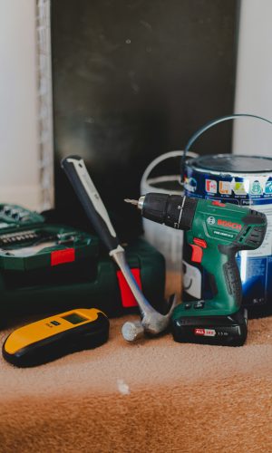 Een foto van een boormachine, verf, een hamer en een gereedschapskist.