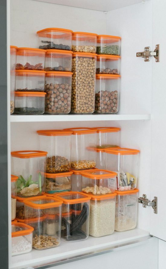 Een opgeruimde keukenkast met verschillende voorraaddozen op elkaar gestapeld.