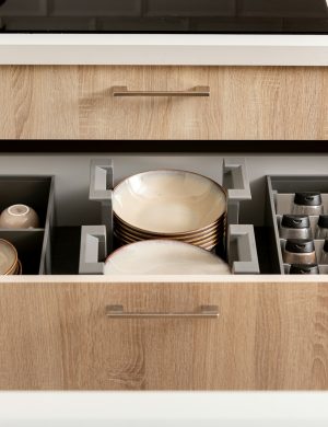 Een georganiseerde keukenlade met borden, mokken en kruidenpotten.