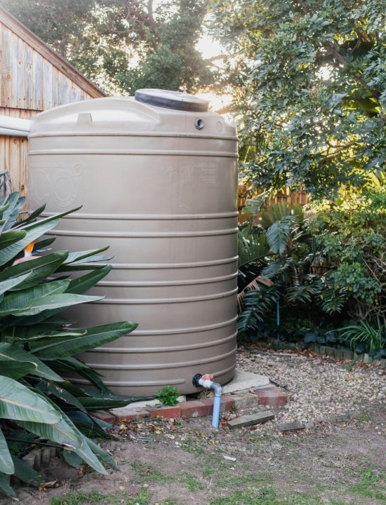Grote bovengrondse regenwaterton in een tuin met een huis op de achtergrond.