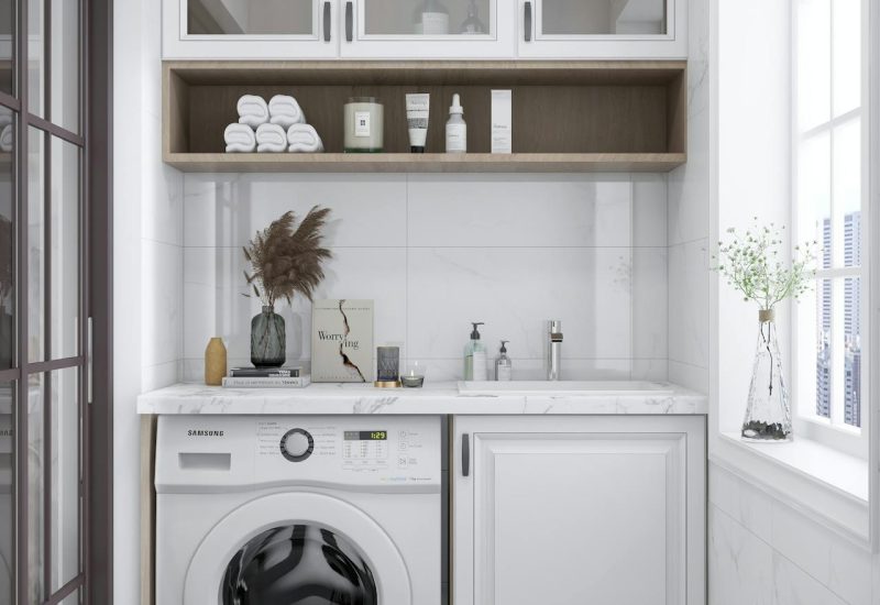 Kleine wasruimte met een wasmachine en een spoelbak ernaast. Erboven hangen kasten en een plank.