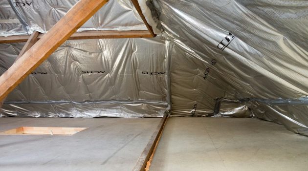 Afbeelding van een dak dat gerenoveerd wordt met zilveren zeilen en zichtbarte delen witte en oranje isolatie die aan de naden van de zeilen uitsteken. Een paar steunbalken zijn ook zichtbaar.