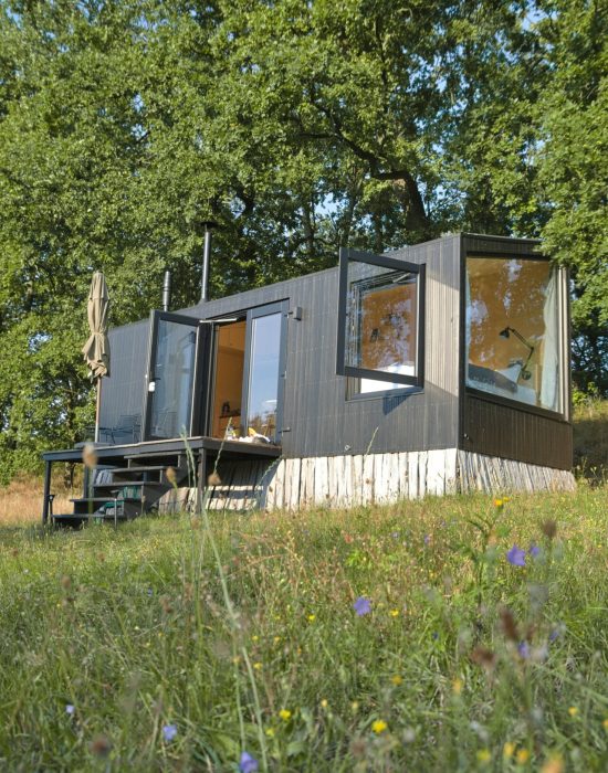 Een tiny house in de vorm van een container in het midden van een veld met de ramen open.