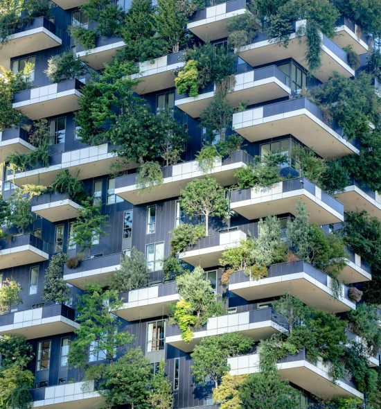 Close-up van een wolkenkrabber met veel groen, struiken en bomen op de gevel.