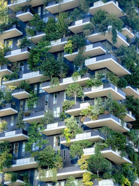 Close-up van een wolkenkrabber met veel groen, struiken en bomen op de gevel.