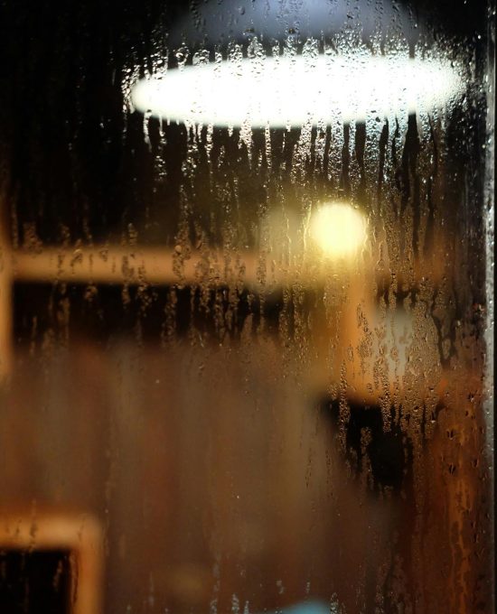 Condens op een raam met op de achtergrond een hanglamp.