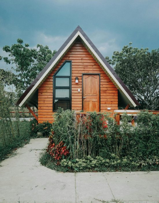 Een klein huis met een houten muur omgeven door struiken.