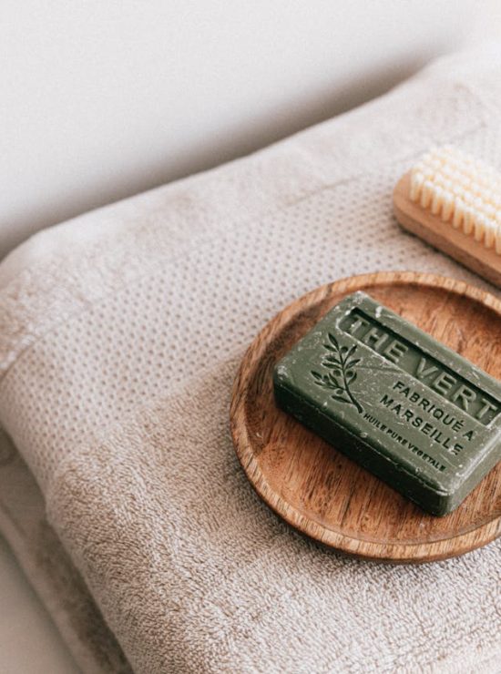 Een zeep op een houten schaaltje die zich op een stapel dikke, witte handdoeken bevinden.