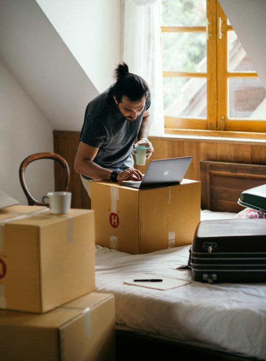 Een man die aan het verhuizen is en iets op zijn laptop opzoekt. De laptop staat op een verhuisdoos.