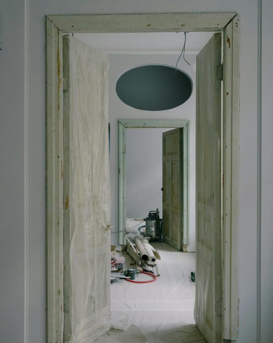 De binnenkant van een huis dat gerenoveerd wordt. Op de foto zie je een open dubbele deur waardoor je kan binnenkijken bij de renovaties.
