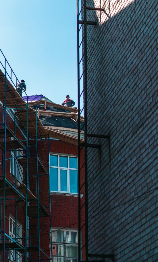 Twee gevels met in de verte twee dakwerkers op het huis aan de linkerzijde die een dakrenovatie aan het uitvoeren zijn.