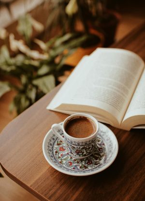 Een geopend boek met daarnaast een mooi versierd koffiekopje op een schotel.