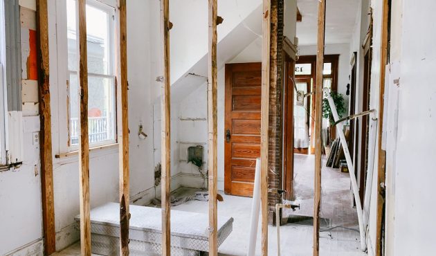 De binnenkant van een woning die gerenoveerd wordt. Je ziet houten palen die een wand moeten worden met ernaast dikke tegels.