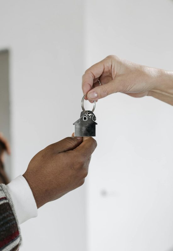Twee handen die een sleutel met een sleutelhanger van een huis aan elkaar doorgeven.