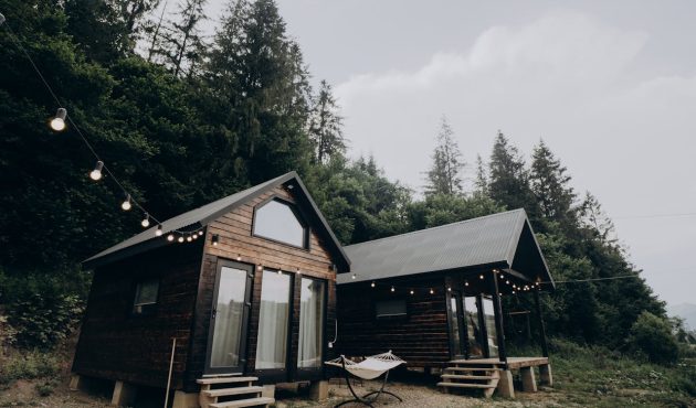 Twee tiny houses gebouwd van hout die zich voor een dennenbos bevinden.