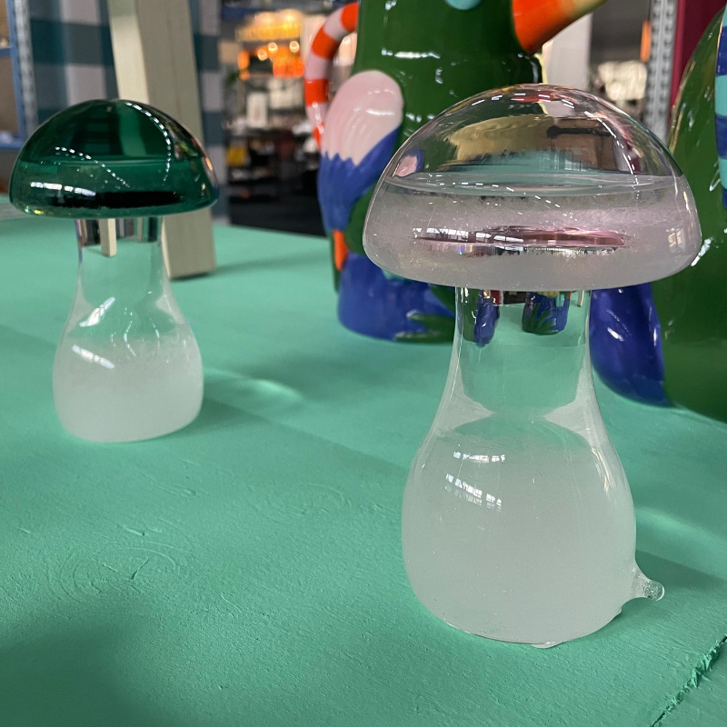 Twee glazen paddenstoelornamenten op een turquoise tafel