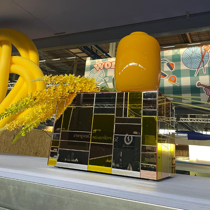 Gele vaas op spiegelende sokkel met bloemen