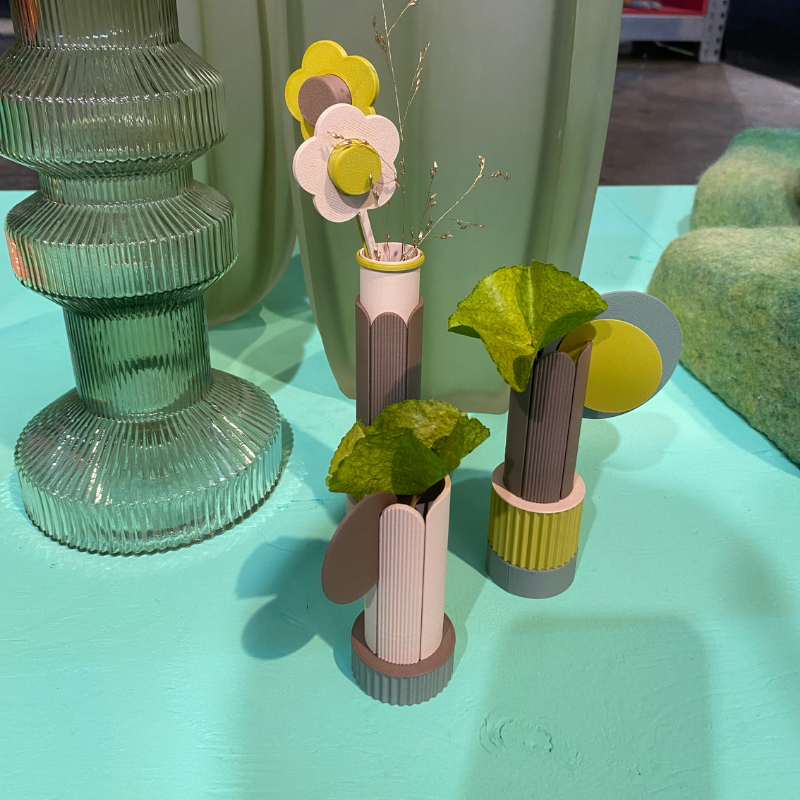 Papieren bloemen in geribbelde vaasjes naast groen glas