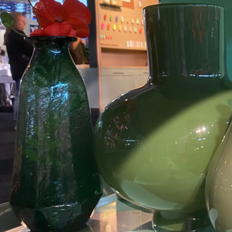 Groene glazen vazen met rode bloemen in interieurwinkel