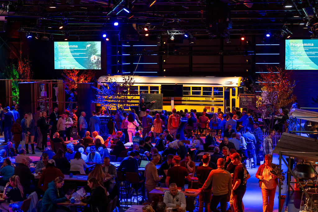 Drukbezocht indoor evenement met gele schoolbus en kleurrijke verlichting