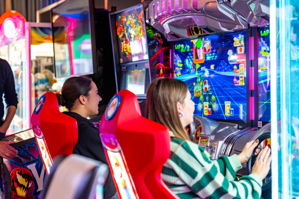 Twee vrouwen spelen Mario Kart in een arcadehal