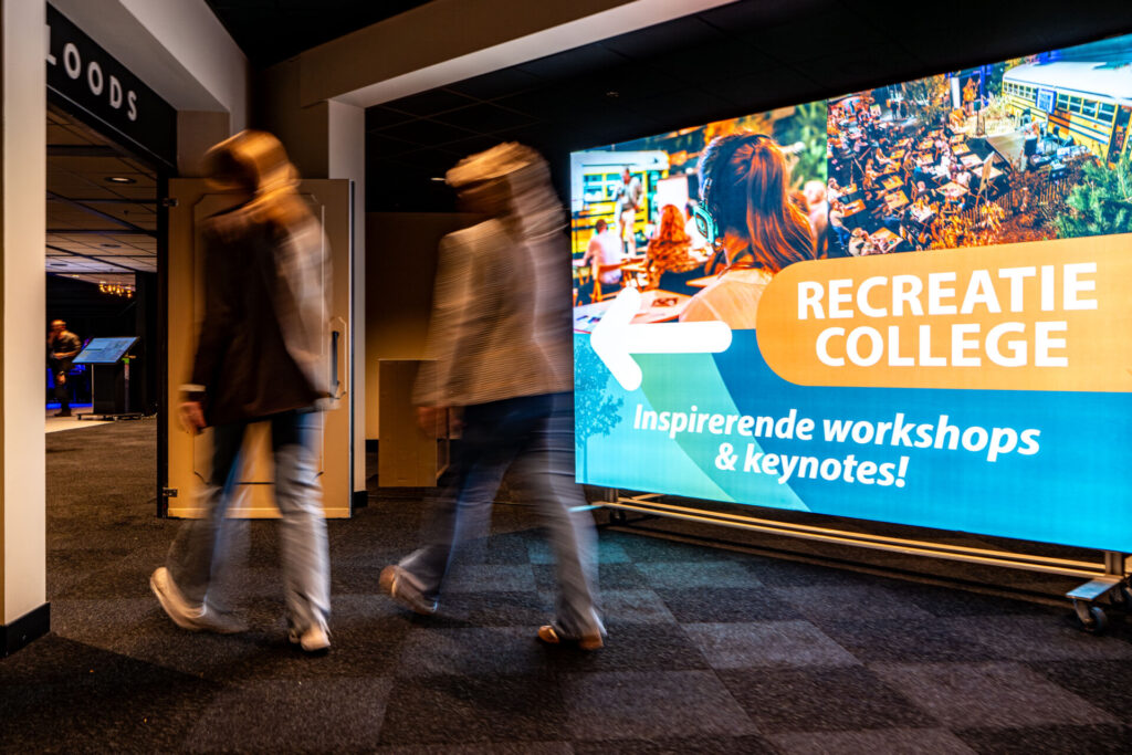 Bezoekers lopen langs bord voor Recreate College