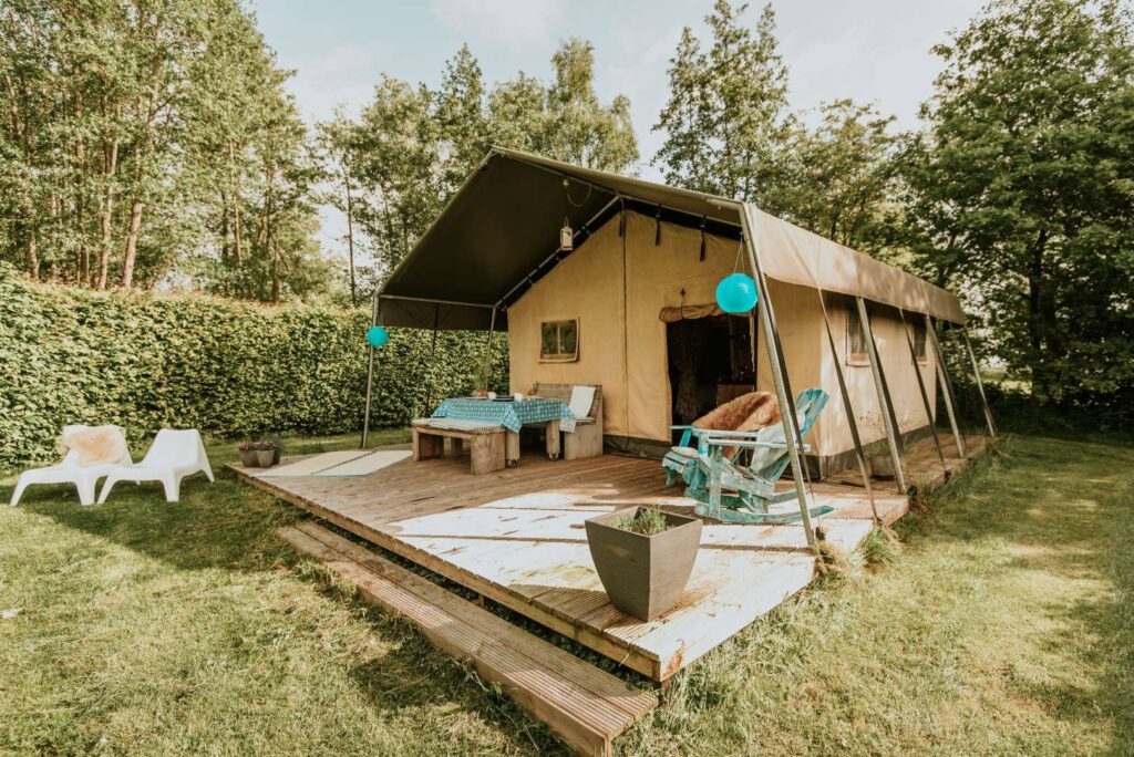 Glampingtent met houten terras in groene bosrijke tuin