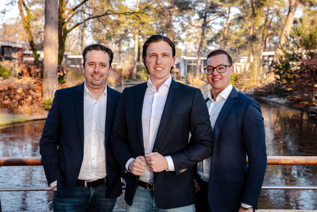 Drie mannen in pakken bij een waterpartij in herfstpark