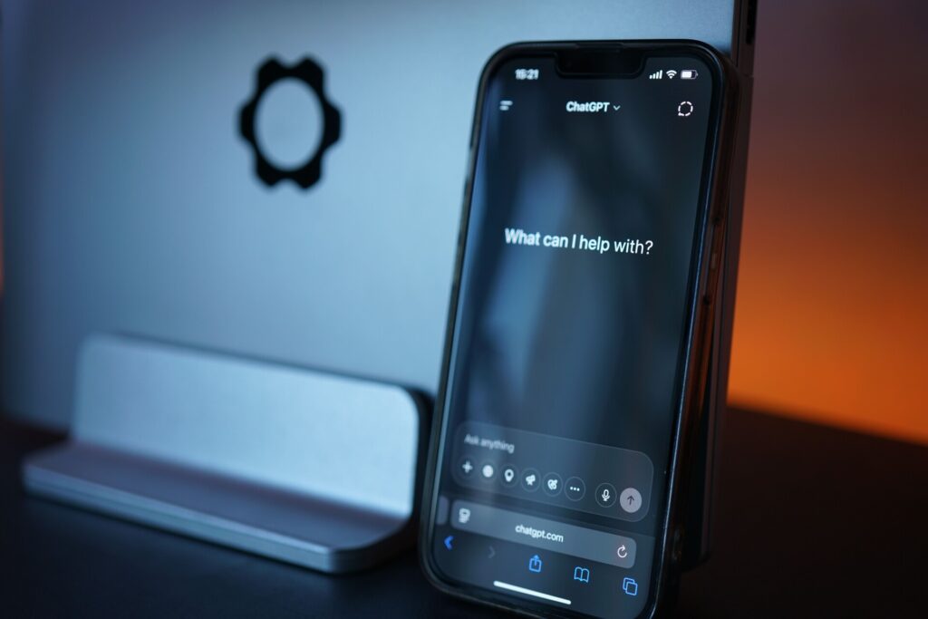 Smartphone met ChatGPT-interface naast laptop op bureau