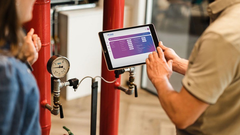 Monteur bedient tablet bij rode verwarmingsleidingen en drukmeter