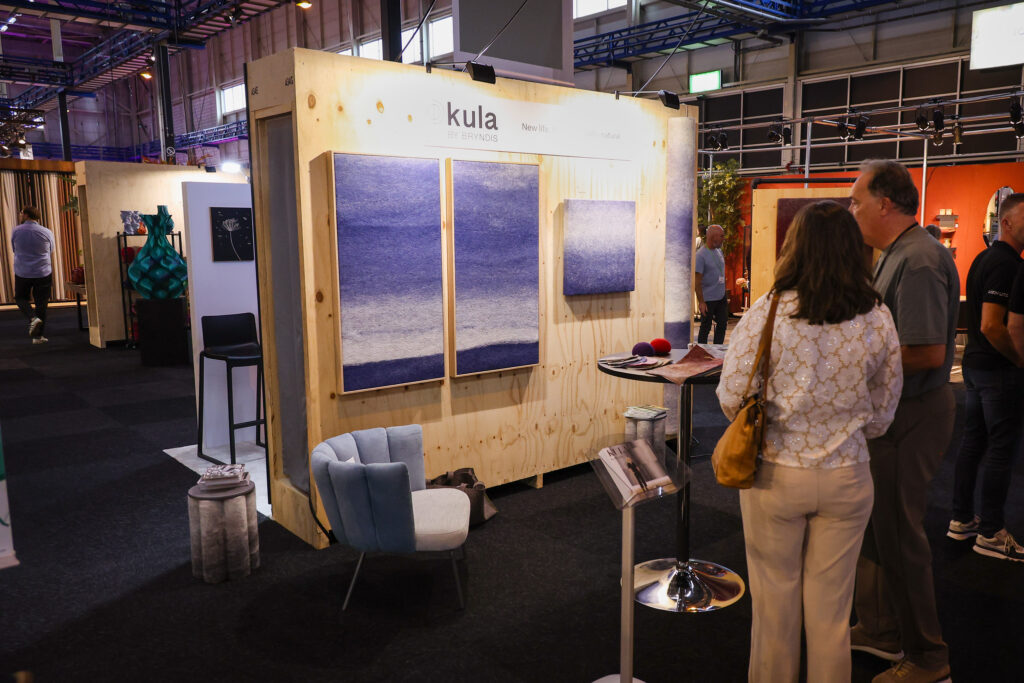 Bezoekers bekijken Kula-stand met blauwe wandpanelen op beurs