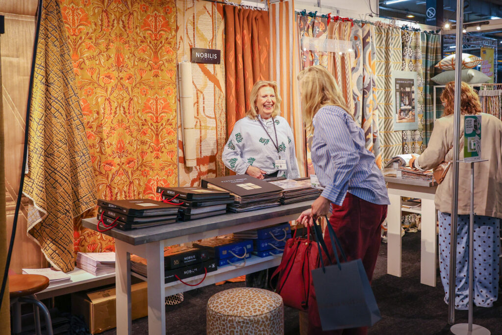 Bezoekers bekijken luxe gordijnstoffen op een interieurbeurs.